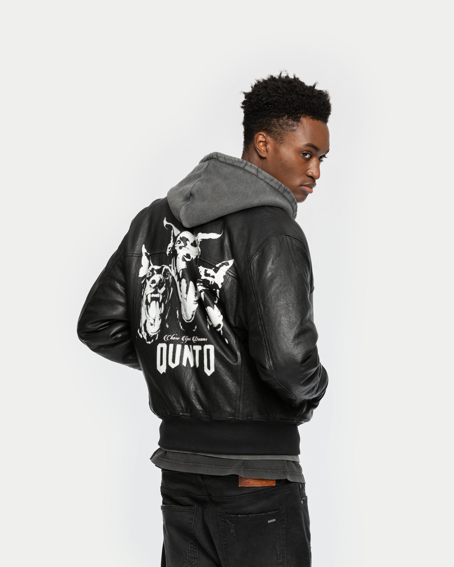 A man wearing a black leather jacket with a high-quality dogs print on the back, side pockets, and ribbed collar.